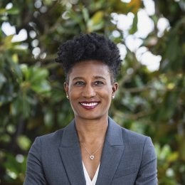 Black woman with short, black hair. Smiling with arms crossed in a gray suit.