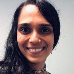 A smiling Brown woman with long hair, nosering and necklaces.