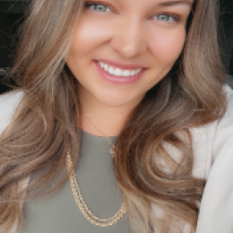 White woman with long brown hair, green eyes and a green top with grey blazer is smilling