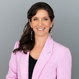 headshot of shanna hirsch - she has long brown hair and is wearing a pink blazer