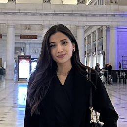 A young woman standing and wearing a black coat.