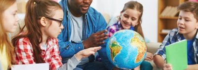 children sitting around teacher and looking at a globe