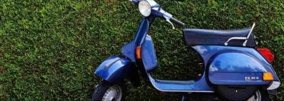 A blue moped leaned against a green hedge.