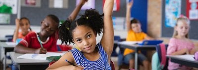 A classroom of children with hands raised