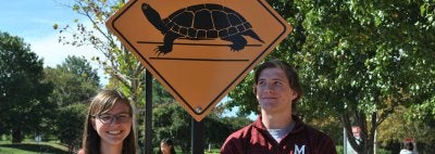 two student ambassadors in front of a turtle crossing sign