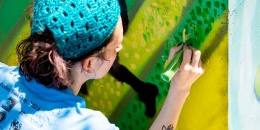 A College of Education graduate student paints an electrical box in the Lakeland community of College Park as part of a community-based art project with Lakeland residents and Clinical Associate Professor Margaret Walker.