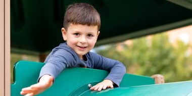 A child smiles while on the big climber on the playground.