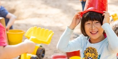 A child smiles while playing with sand toys on the playground.