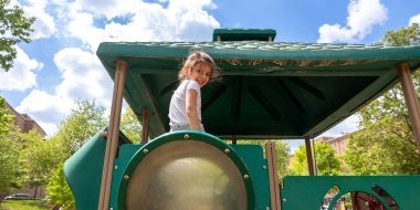 A child smiles while on the big climber on the playground. 