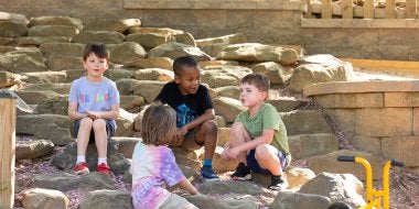 Children sit on rock steps on the playground.