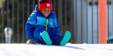 A child prepares to slide down a snowy hill on the playground.