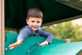 A child smiles while on the big climber on the playground.
