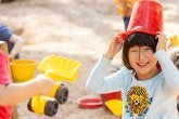 A child smiles while playing with sand toys on the playground.