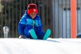 A child prepares to slide down a snowy hill on the playground.