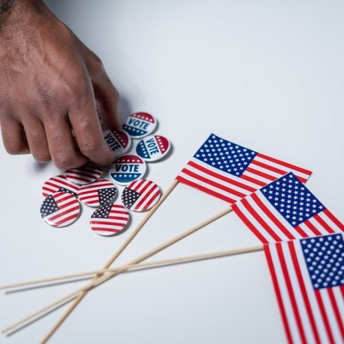 Miniature American flags and voting buttons on a table. Hand reaching towards buttons