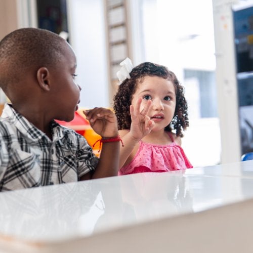 A little girl in a classroom holds up three fingers.