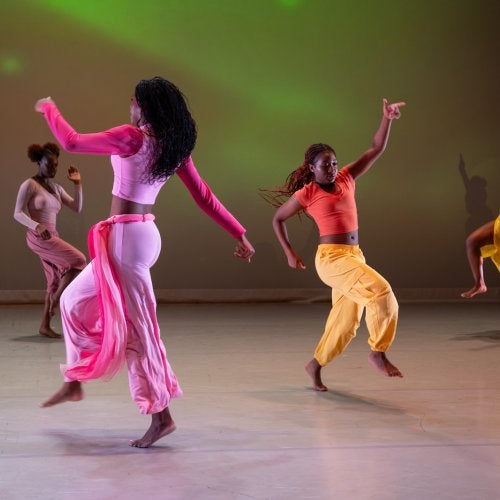 Four dancers dressed in bright colors dance across a stage.