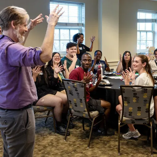 Michael Dunham, lecturer and program director for UMD's American Sign Language minor, applauds with students at a signing dinner, where everyone communicated solely by using ASL.