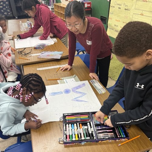 Associate Professor Cixin Wang helps two third graders at Brandywine Elementary School create posters as part of the Bullying Literature Project.