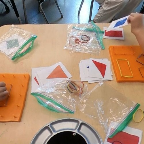 A close-up image of children's hands as they use rubber bands on geoboards to make various shapes.