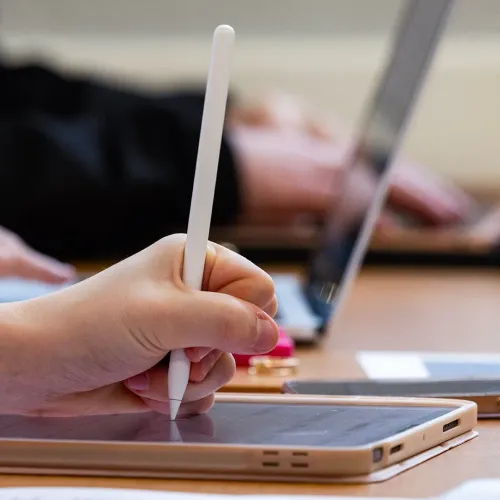 Close-up of a student's hand holding a stylus and using a tablet.