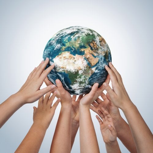 Multiple pairs of hands hold up a world globe.