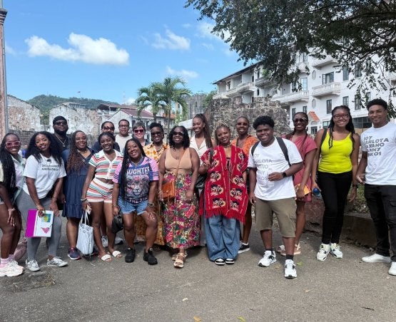 A group picture from the study abroad course in Panama, January 2026, with white and stone buildings and a palm tree in the background.