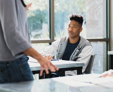A teacher speaks to two Black students in a classroom.