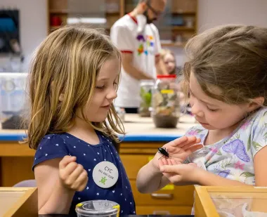 Center for Young Children (CYC) kindergarteners Abigail Lynn and Nora Hurst examine a Bess beetle during a field trip to UMD's Insect Zoo.