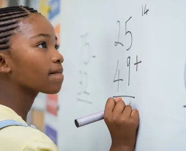 A student works on a math problem at a whiteboard.