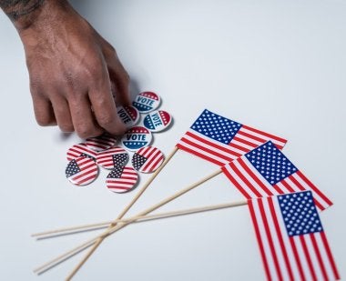 Miniature American flags and voting buttons on a table. Hand reaching towards buttons