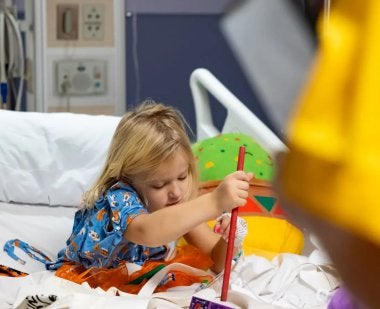 A young hospital patient plays a musical instrument brought by music education major Paige Peercy ’25. Photo by Riley Sims Ph.D. '23