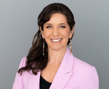 headshot of shanna hirsch - she has long brown hair and is wearing a pink blazer