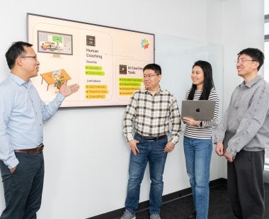 A man in a classroom pointing to a board teaching 3 students a lesson. 