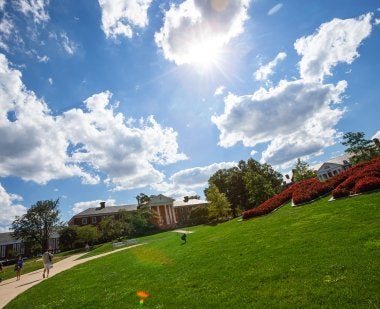 The "M" on the UMD campus blooms with red flowers, with a blue sky and white clouds above.
