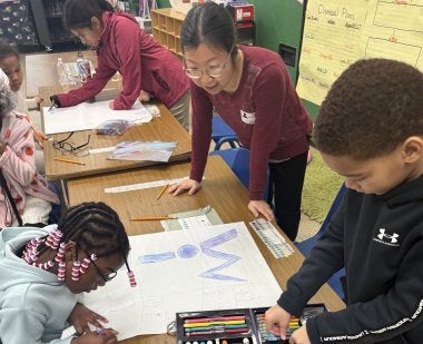 Associate Professor Cixin Wang helps two third graders at Brandywine Elementary School create posters as part of the Bullying Literature Project.