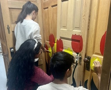 Students in the community-based art course HNUH278Q paint the doors that make up the main structure of the community art project.