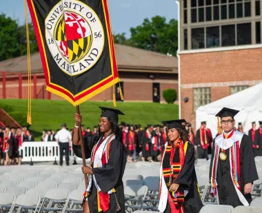 Senior marshals march and carry banners at UMD's main Commencement ceremony.