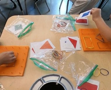 A close-up image of children's hands as they use rubber bands on geoboards to make various shapes.