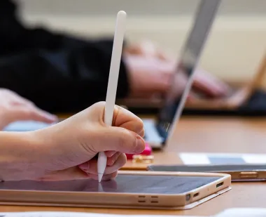 Close-up of a student's hand holding a stylus and using a tablet.