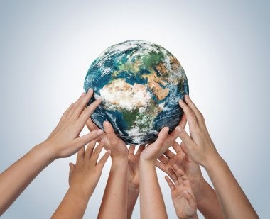 Multiple pairs of hands hold up a world globe.