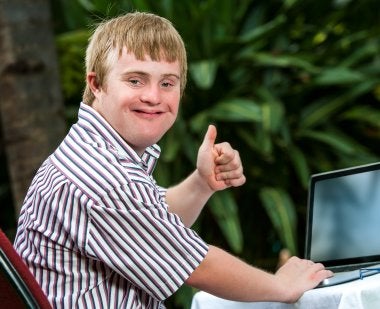 Young man with disability gives thumbs up while working on computer