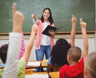 teacher in classroom with students hands raised