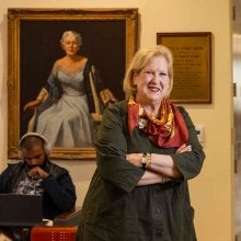 Marsha Guenzler-Stevens stands in front of a portrait of Adele Stamp