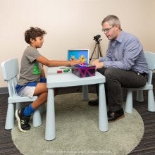 Luke Butler and child in lab, child adding toy to box with computer monitor adjacent