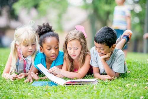 Four Children Lying in Grass Reading Book