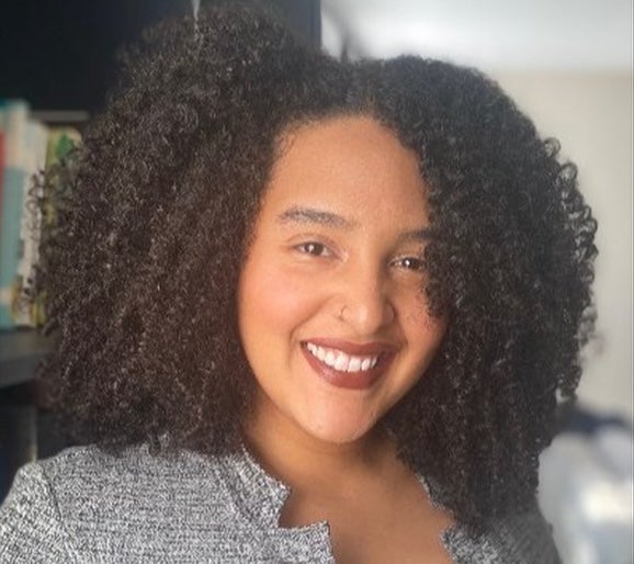 Headshot of a smiling, Afro-Latina, female-presenting woman with mid-length curly hair