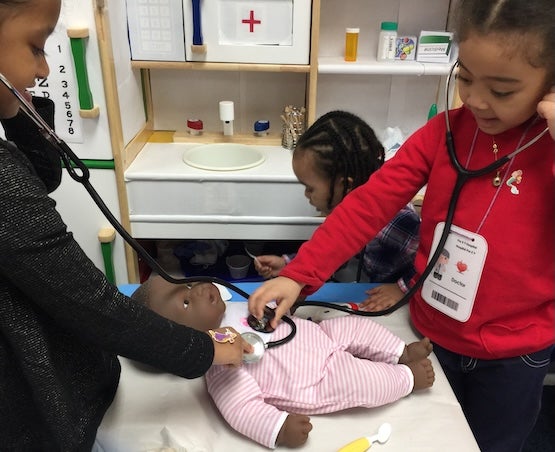 Two girls using stethoscopes on baby doll