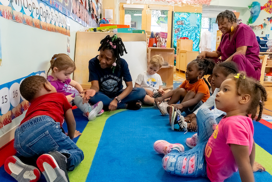 Two Educators With Children In Circle In Classroom