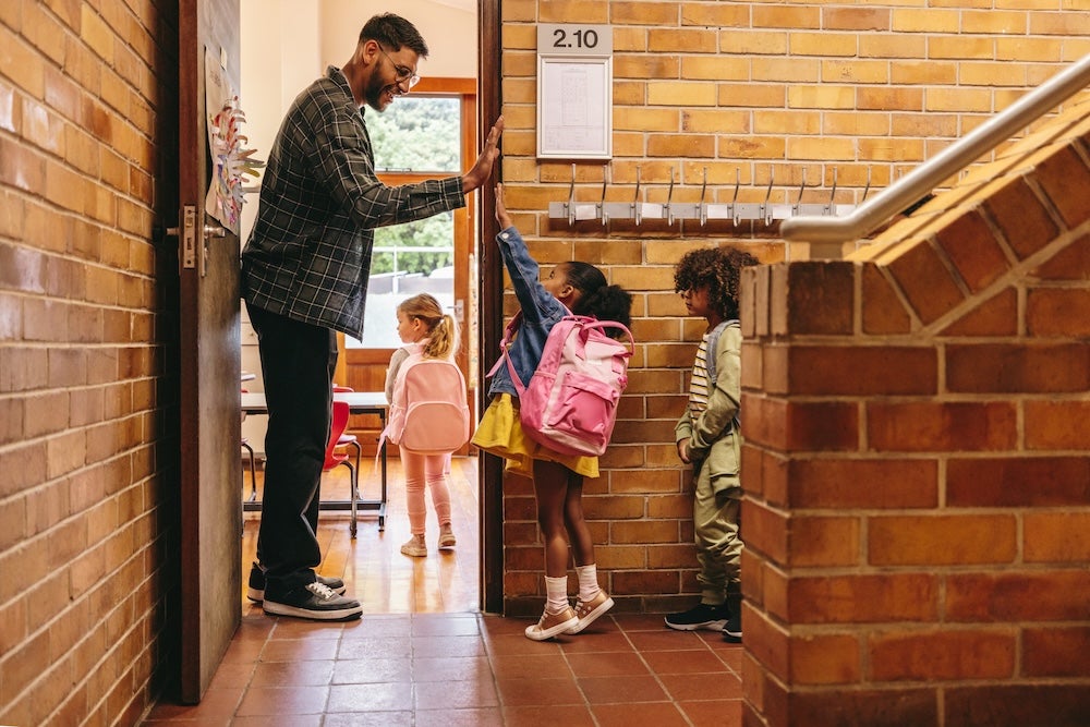 Male teacher greeting children at classroom door